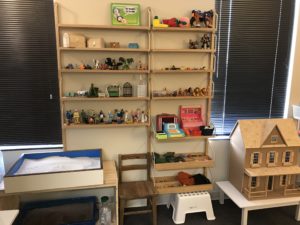 Ladybug Counseling Play Therapy_Rita Stevermer_Image of wooden shelves with toys, a dollhouse, and a sand tray