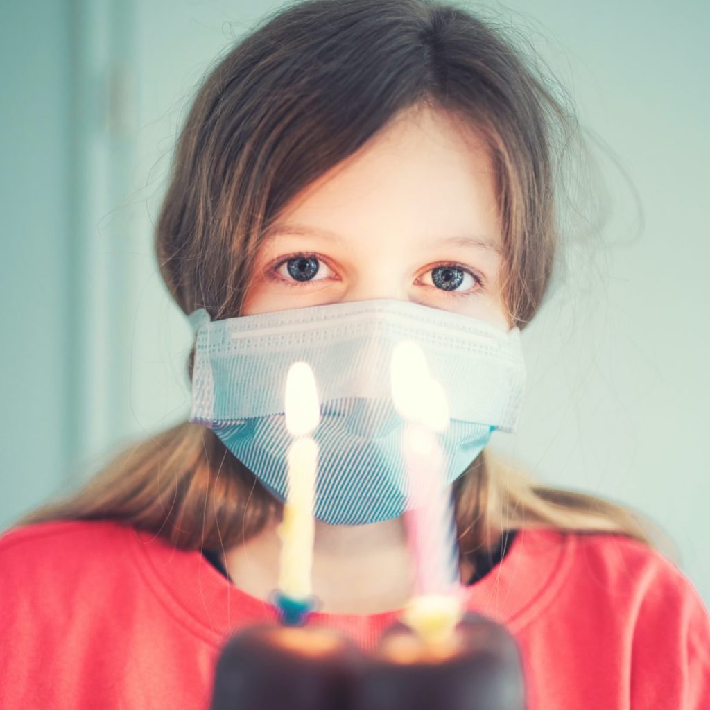 help kids navigate the COVID-19 pandemic; image is of a young girl wearing a face mask and holding a birthday treat with lit candles