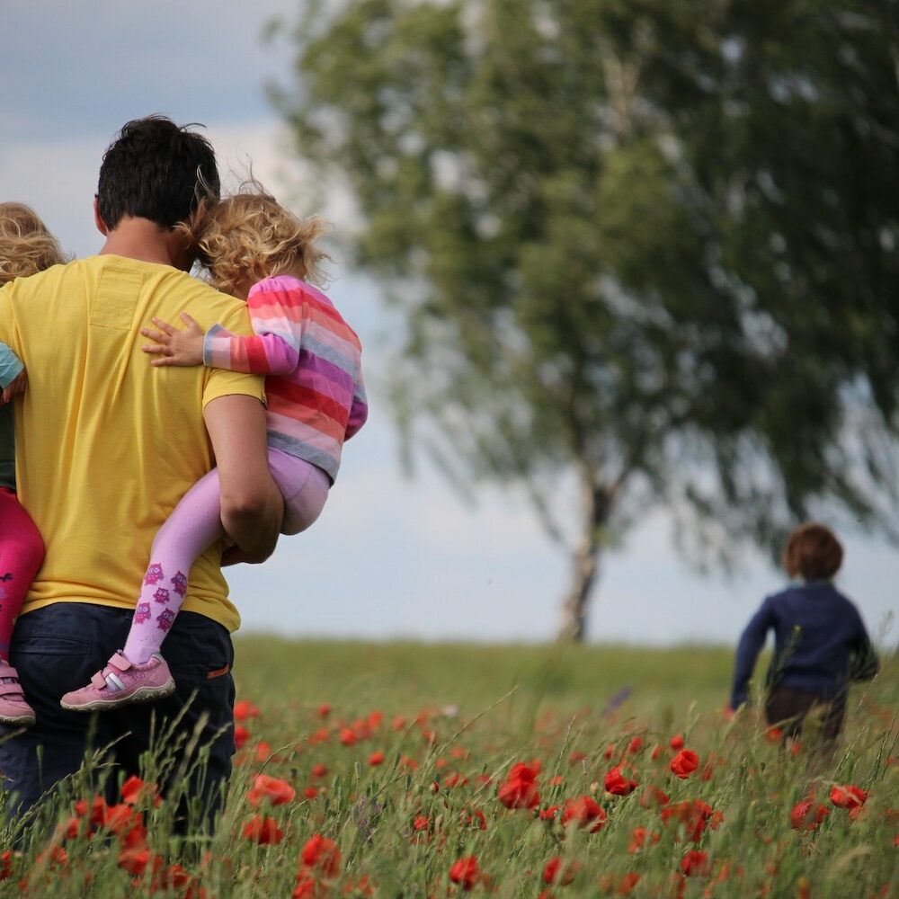 Get Started with Ladybug Counseling_A dad with a yellow shirt and brown hair walks through a field of flowers with his small kids
